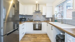 A modern kitchen with stainless steel appliances, white cabinets, a built-in oven, and a window with blinds. - The Lake Hub (Dagenham)