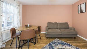 A living room with a sofa, a dining table with chairs, a window with curtains, and a light fixture. - The Lake Hub (Dagenham)