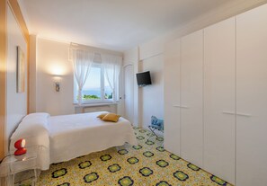 Een slaapkamer met een bed, een aan de muur bevestigde televisie en een raam met gordijnen.