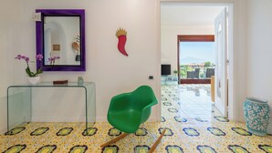 A modern interior with a glass console table, a green chair, a decorative wall piece, and a view through an open door. - Amazing apt with breathtaking seaview&Vesuvius in Sorrento center near the beach (Sorrento)