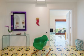 Een modern interieur met een glazen consoles, een groene stoel, een decoratief wandobject en uitzicht door een open deur.