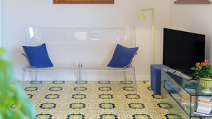 A room with a clear plastic chair, a framed picture on the wall, a television, and a patterned floor. - Amazing apt with breathtaking seaview&Vesuvius in Sorrento center near the beach (Sorrento)