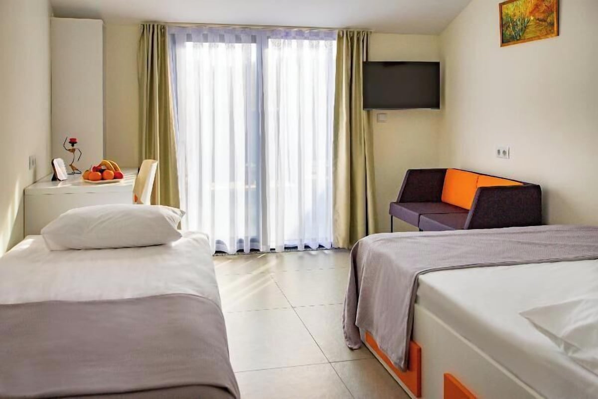 Habitación de hotel con dos camas, un escritorio con silla, televisor de pantalla plana en la pared y ventana con cortinas.