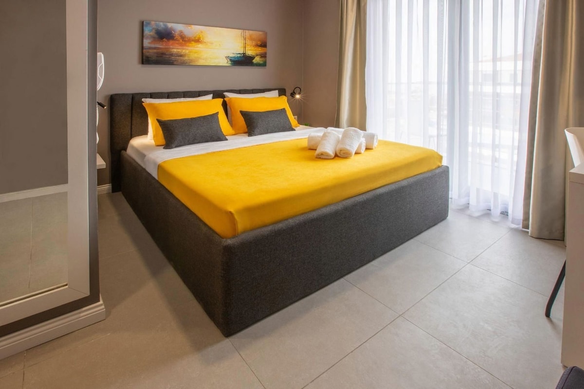 Una cama con estructura gris, una colcha amarilla y dos almohadas.