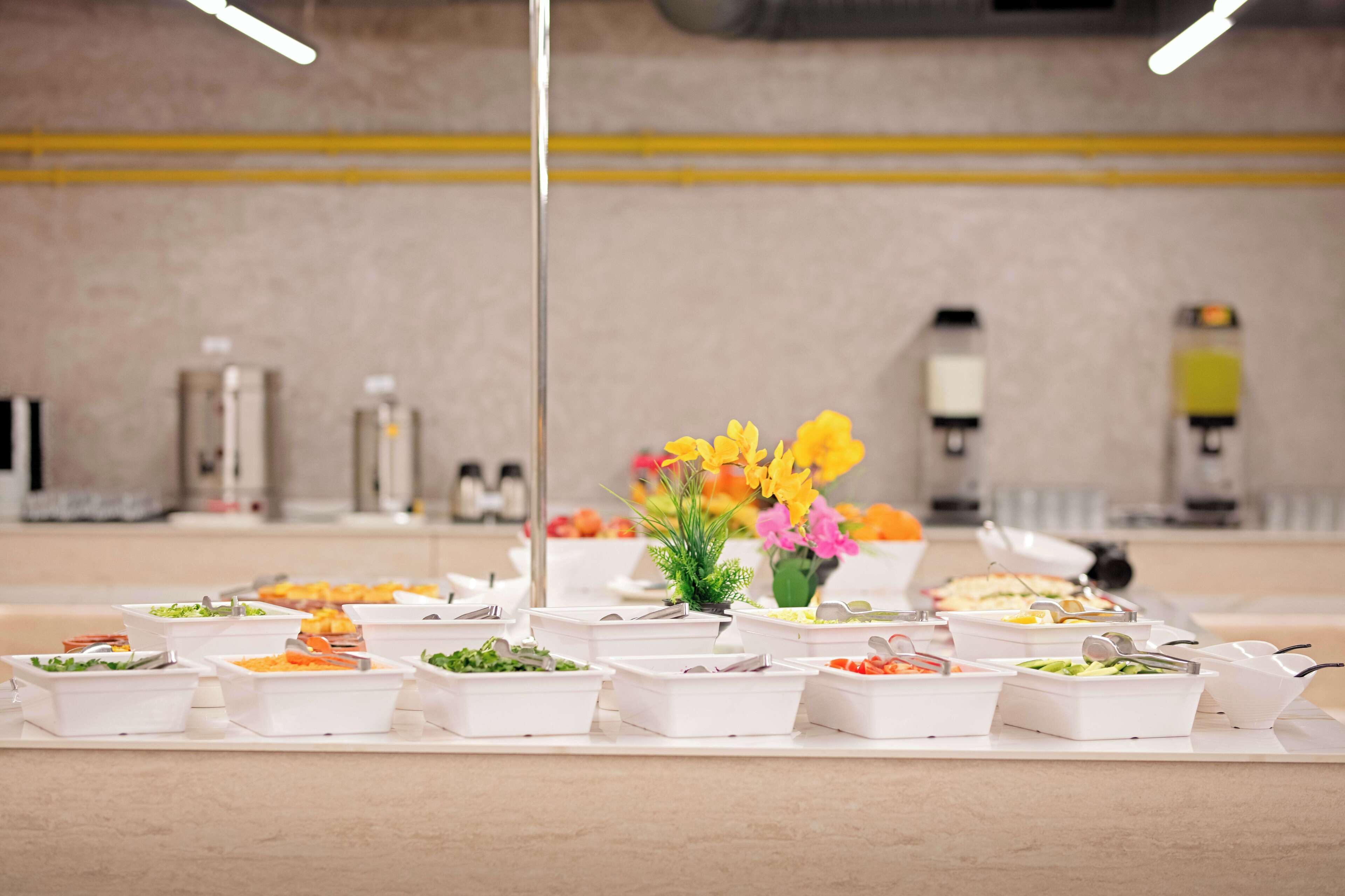 A buffet setup with various food containers and a vase of flowers.