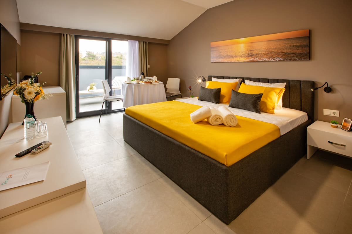 Een moderne hotelkamer met een groot bed, een bureau met een bloevas, een tafel met ontbijtartikelen en een balkon met uitzicht.