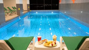 An indoor swimming pool with lounge chairs and a table with food and drinks. - First Joy Hotel (Trabzon)