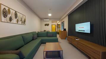 A modern living room with a sectional sofa, a wooden coffee table, and a flat-screen TV displaying "WELCOME".