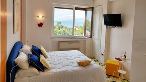 Quarto com cama, janela com vista, televisão e uma pequena mesa com objetos.