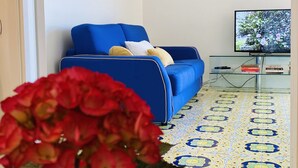 Uma sala de estar com um sofá azul, uma televisão e um piso estampado.