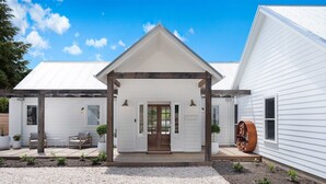 Een wit huis met een overdekte veranda, een houten bank en een grote plantenpot.