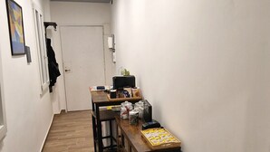 A narrow hallway with a wooden floor, a bench, a desk with a computer, and a door at the end. - Tribunali Platamon (Naples)