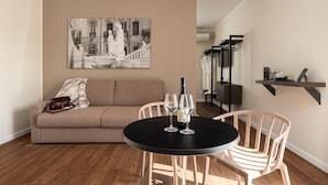 A living room with a beige sofa, a black round table with two wine glasses, and a painting on the wall. - Attico 37 Apartments (Palermo)