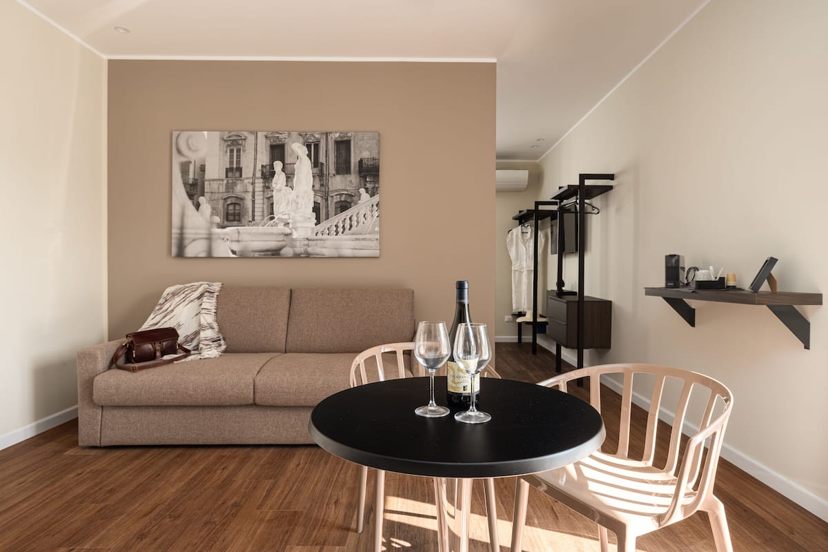 Un salón con un sofá color beige, una mesa redonda negra con dos copas de vino y un cuadro en la pared.