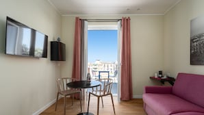 A room with a large window, a flat-screen TV, a pink sofa, and a small table with a cup and saucer. - Attico 37 Apartments (Palermo)
