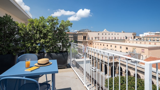 A balcony with a table, chairs, and a view of the cityscape. - Attico 37 Apartments (Palermo)