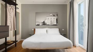 Ein modernes Hotelzimmer mit einem großen Bett, Holzboden, einem Wandbild, einem Nachttisch und Blick ins Freie durch ein Fenster.
