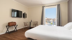 A hotel room with a bed, a TV, a small table with chairs, a suitcase, and a balcony with a view of buildings. - Attico 37 Apartments (Palermo)