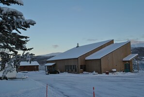 A large building with a sloped roof, surrounded by snow-covered ground and trees.