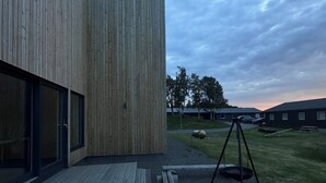 Un edificio moderno con fachada de madera, un área de estar al aire libre cubierta y suelo de grava.