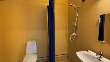A small bathroom with a toilet, a shower with a curtain, a sink, and a mirror.