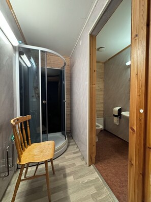A compact bathroom with a shower, toilet, and a wooden chair.