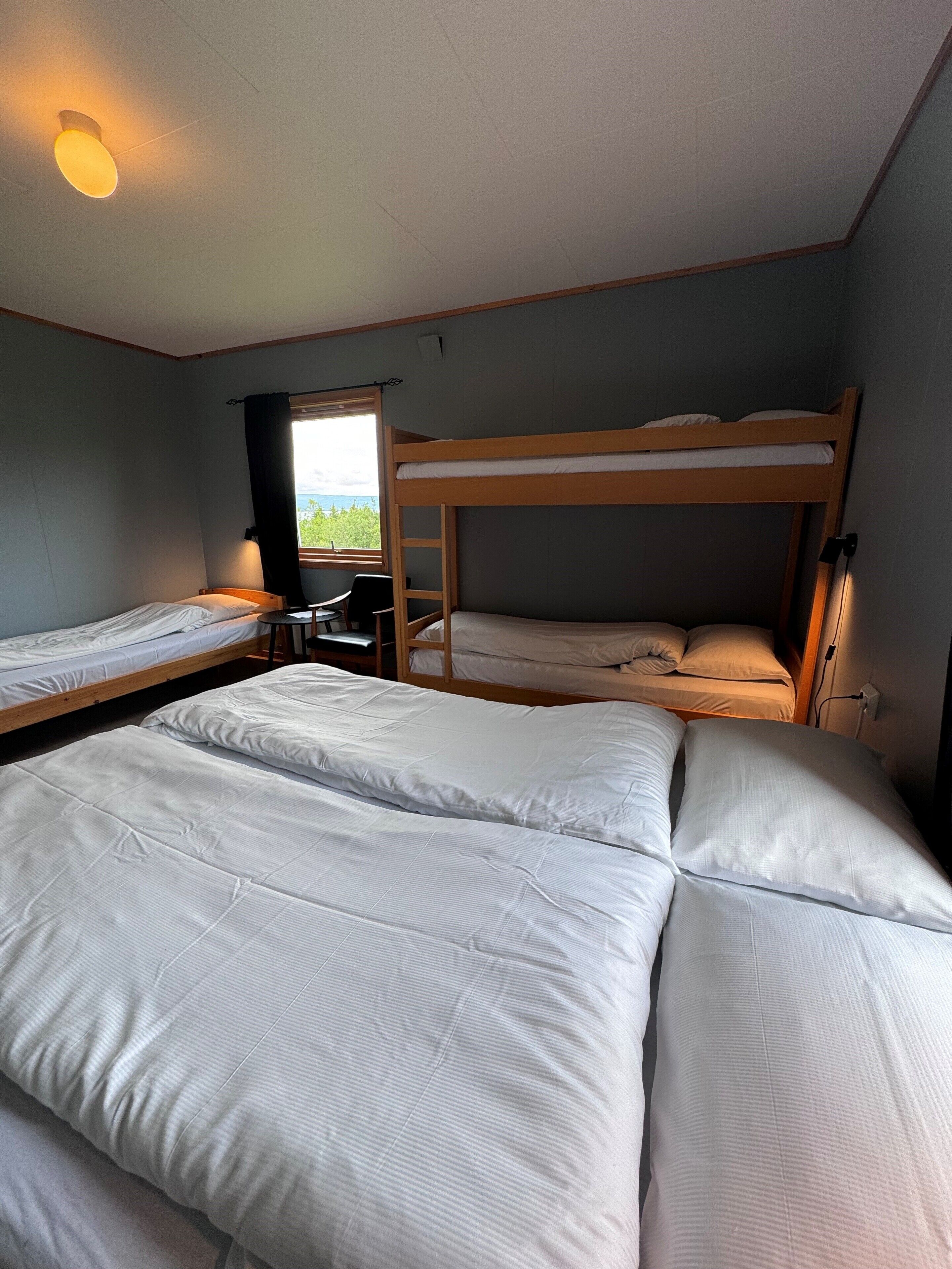 A dormitory room with bunk beds, a desk, and a window with curtains.