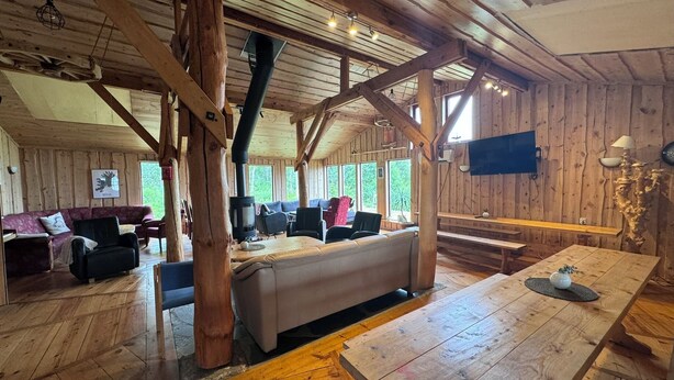 Interior rústico de una cabaña con suelo de madera, un sofá, una mesa y una chimenea.
