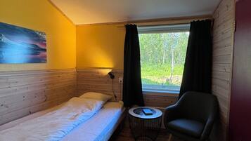 Una habitación pequeña con cama, una silla, una mesa y una ventana con cortinas.