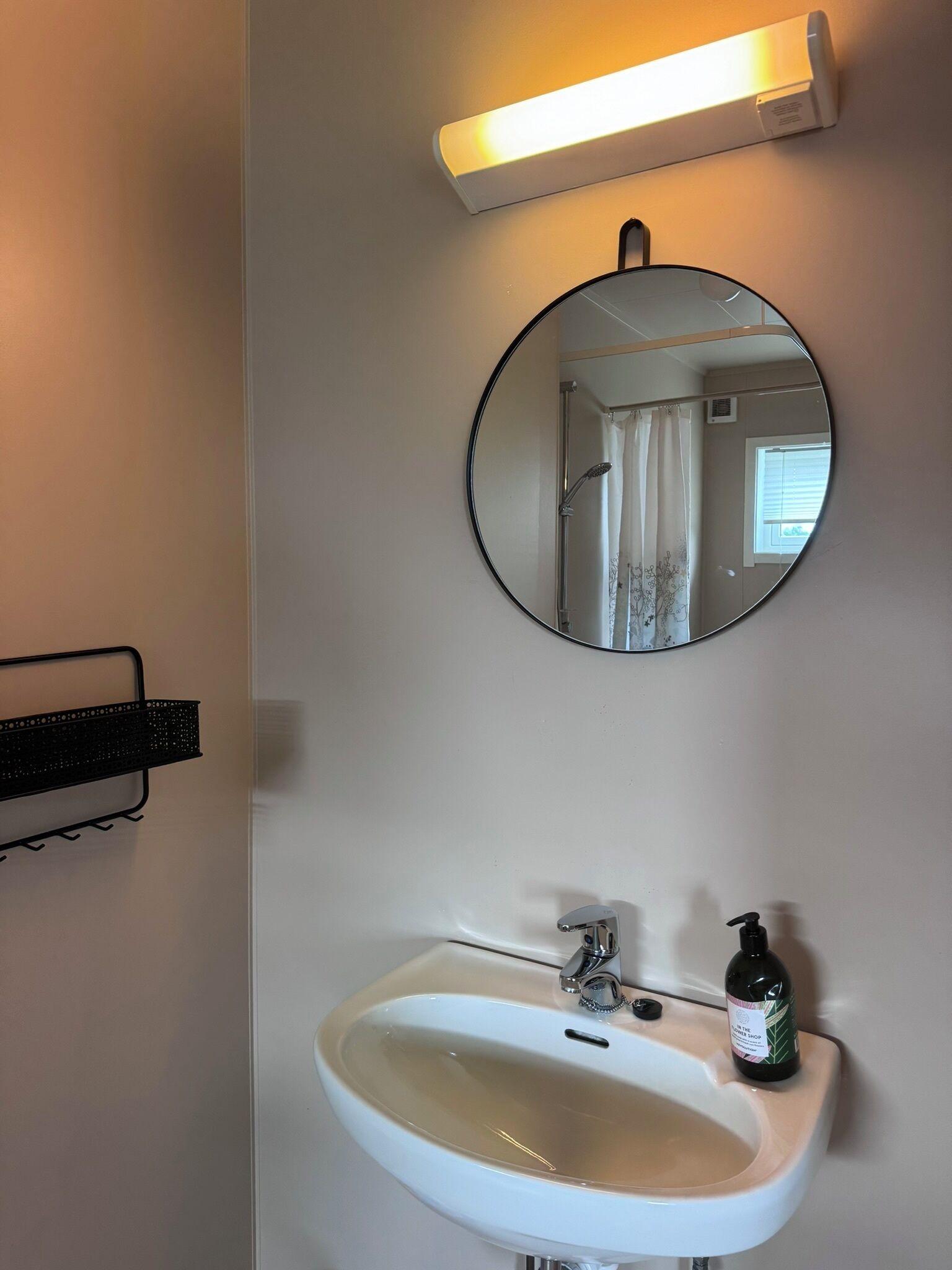Un baño con un lavamanos blanco, un espejo redondo y un calentador de pared.