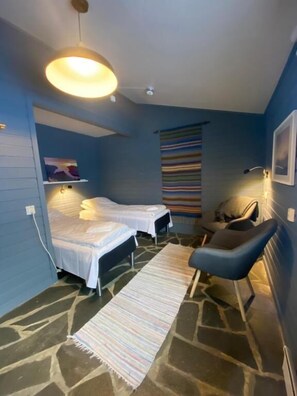 A compact room with two beds, a chair, a rug, and a striped wall hanging.