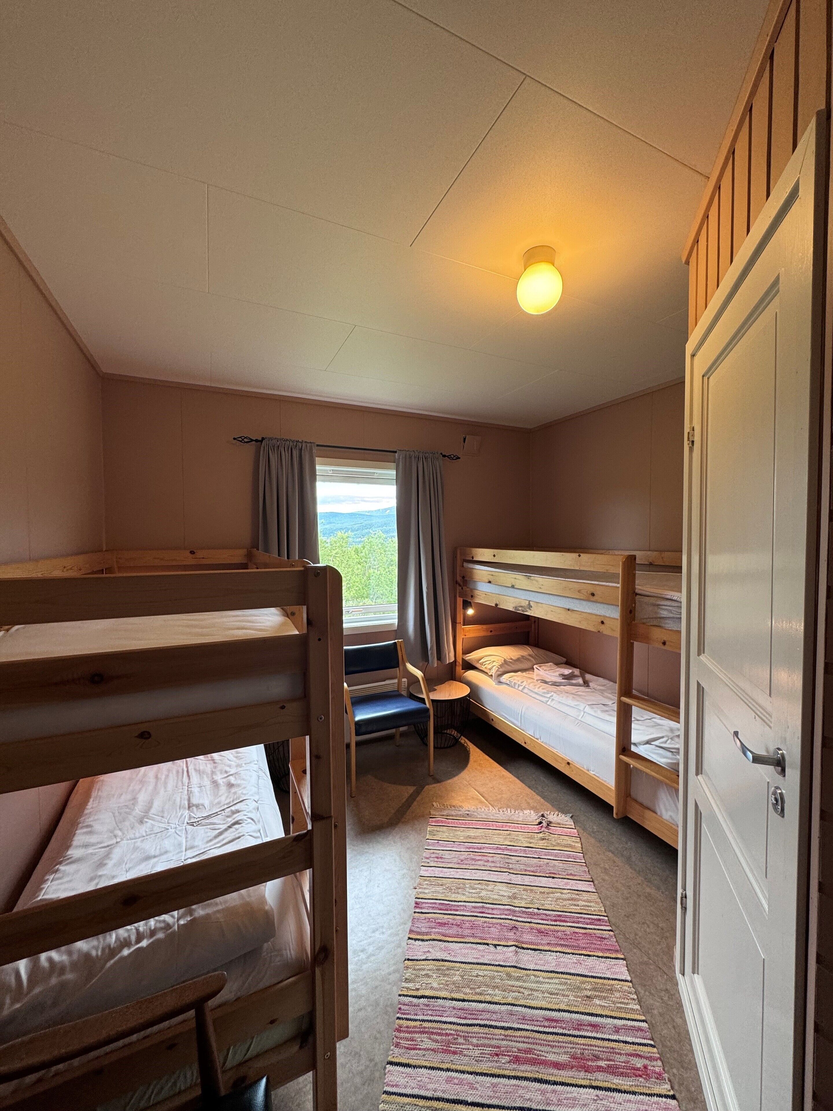 A room with bunk beds, a desk, a chair, a window with curtains, and a door.
