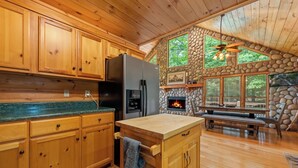 A wooden cabin kitchen with stone walls, a stone fireplace, and a large dining table. - Sunset in the Mountains – Blue Ridge, GA. (Blue Ridge)