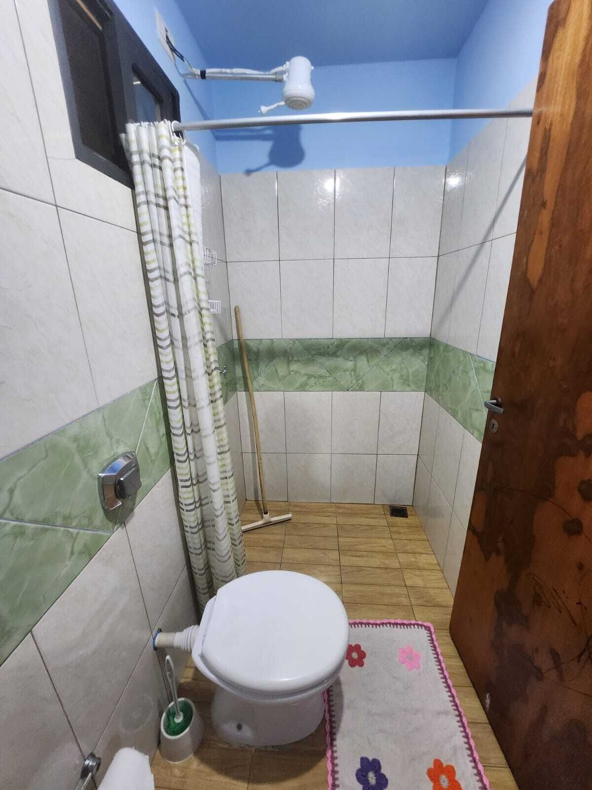 Ein kleines Badezimmer mit Toilette, Duschvorhang, einem Mopp und einer Fußmatte.