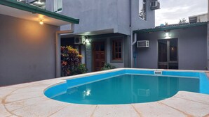 A swimming pool with a curved edge, surrounded by a tiled deck. There are plants and a door visible in the background. - El Rinconcito Iguazú (Puerto Iguazú)