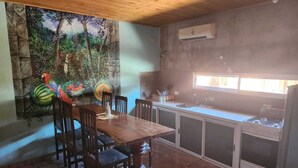A dining area with a wooden table and chairs, a kitchen with a stove and cabinets, and a mural of a forest scene on the wall. - El Rinconcito Iguazú (Puerto Iguazú)