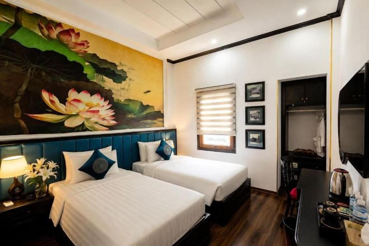 Una camera d'albergo con due letti, un quadro grande con fiori di loto, un armadio e una televisione.