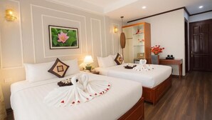 Une chambre d’hôtel avec deux lits, chacun décoré d’un cygne en serviette et de pétales de rose. On y trouve un bureau avec un miroir et un vase de fleurs.