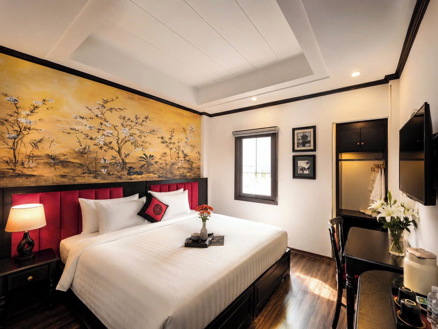 A hotel room with a large bed, a painting on the wall, a window, a desk, and a television.