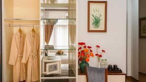 Une chambre d’hôtel dotée d’une douche en verre, d’une coiffeuse avec un miroir, d’une œuvre d’art florale encadrée et d’un vase rempli de fleurs rouges.
