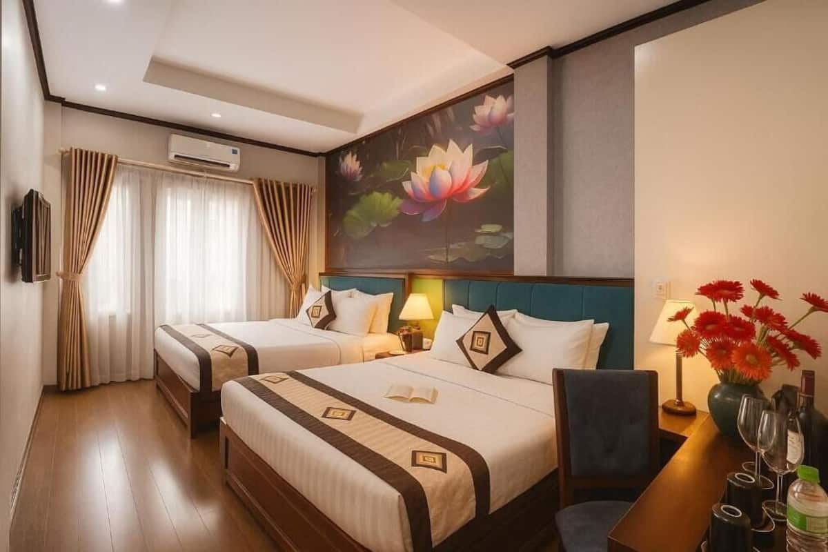 Une chambre d’hôtel avec deux lits, un grand tableau représentant des fleurs de lotus, un téléviseur à écran plat et un bureau agrémenté d’un vase de fleurs.