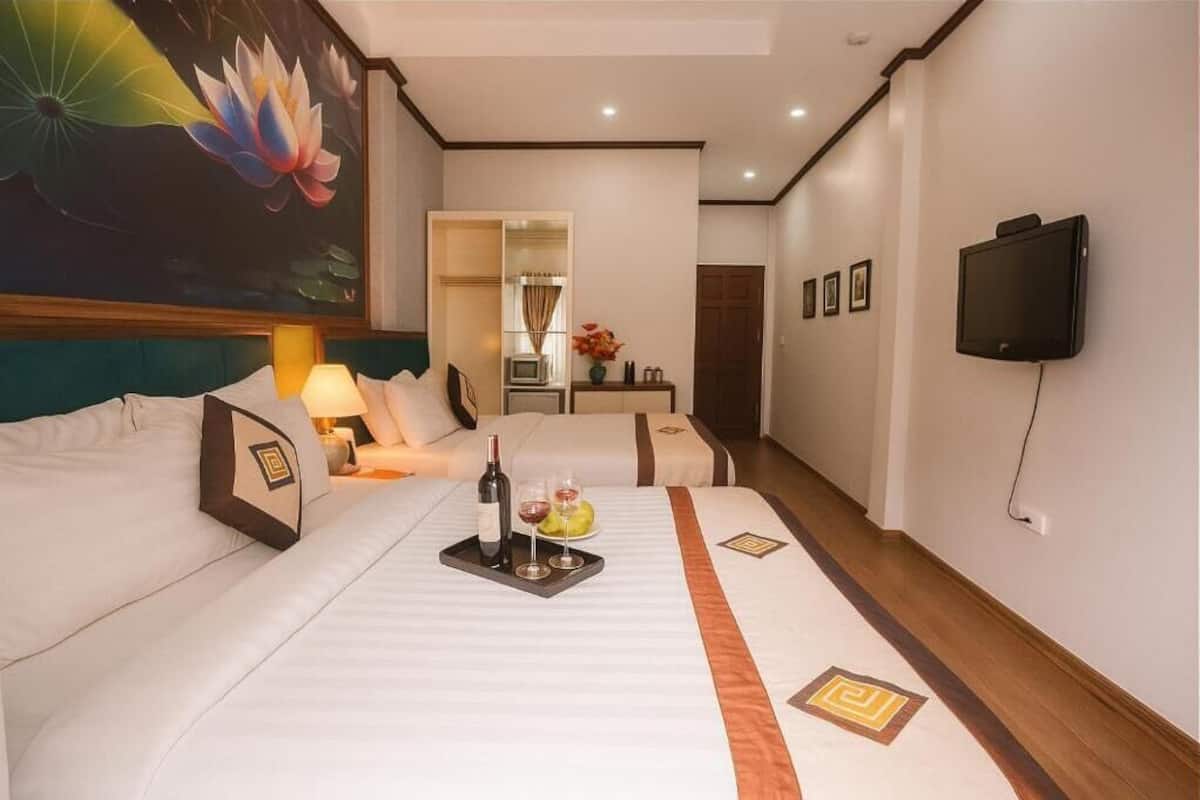 Une chambre d’hôtel avec un grand lit, un plus petit lit, une télévision, un tableau représentant des fleurs de lotus et un miroir.