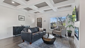 A modern living room with a gray sofa, a round coffee table, and a large window with a view of the outdoors. - DerbyGrove: Newly Renovated & Near Derby (Jeffersonville)