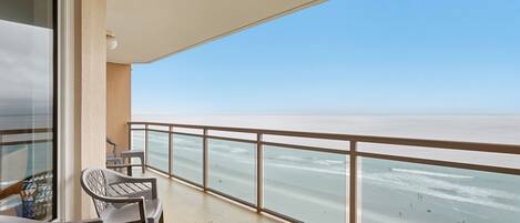 A balcony with a view of the sea, a table, and two chairs.