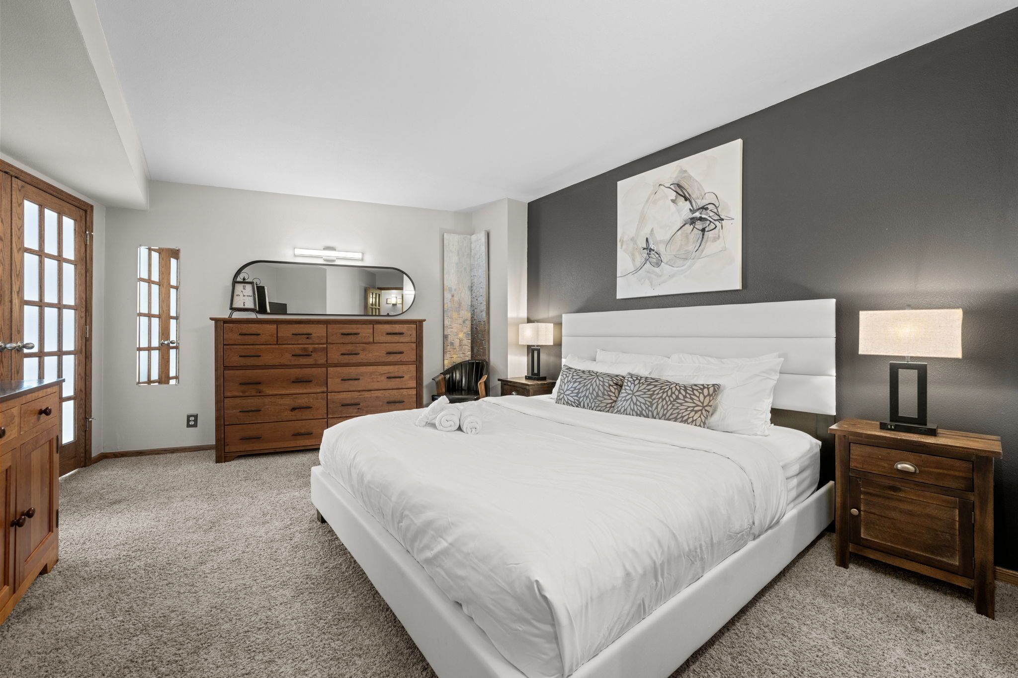 A bedroom with a large bed, wooden dresser, nightstands, and a wall-mounted mirror.