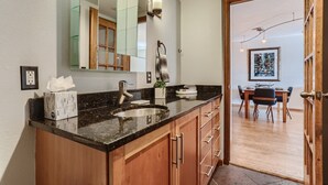 A modern bathroom with a granite countertop, a sink, and wooden cabinets. There is a mirror above the sink and a wall-mounted light fixture. - Condo in the Sky - Amazing Views - Gym (denver)