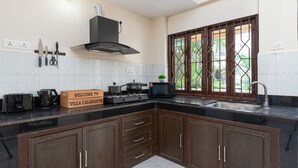 A kitchen with dark wooden cabinets, a black countertop, a stove, a microwave, and a sink. There is a welcome sign and a window with a view of greenery. - Villa Calangute Phase 7 (Candolim)