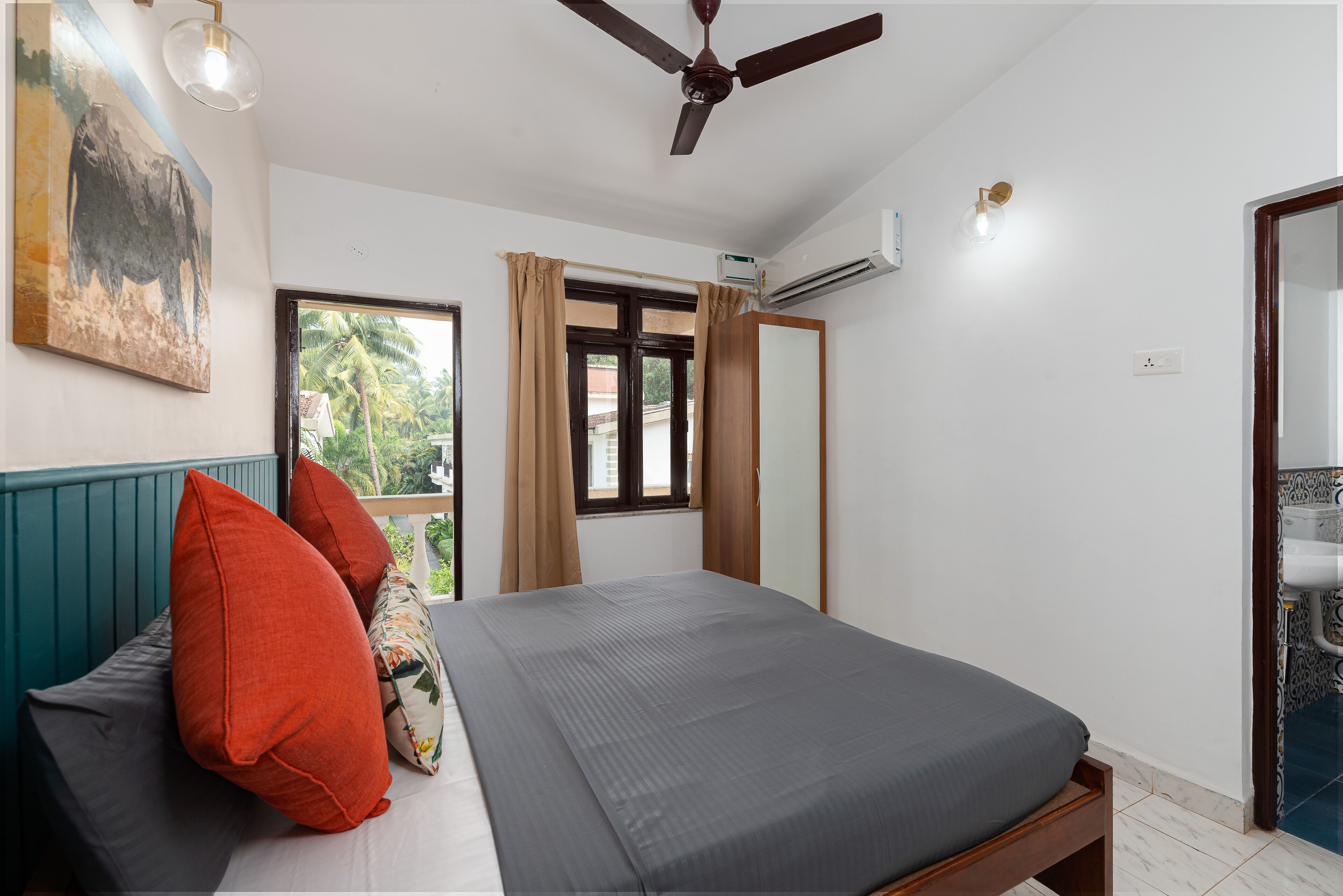 A bedroom with a bed, a ceiling fan, a window with curtains, an air conditioning unit, and a bathroom with a sink.