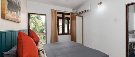 A bedroom with a bed, a ceiling fan, a window with curtains, an air conditioning unit, and a bathroom with a sink.