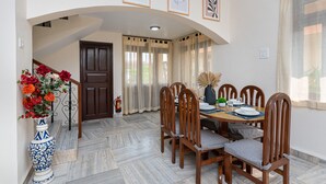 A dining area with a wooden table, chairs, and a vase of flowers. - Villa Calangute Phase 7 (Candolim)